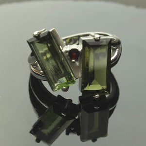 May include: A silver ring with two green rectangular gemstones and a small red gemstone.