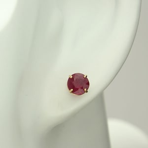 May include: A pair of gold stud earrings with a single round red ruby gemstone in each earring.