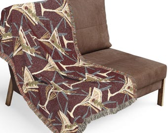 May include: A woven throw blanket featuring a repeating pattern of martini glasses with olives on a deep burgundy background. The blanket has a textured, fringed edge and displays a geometric design of light-colored glasses against the dark fabric.