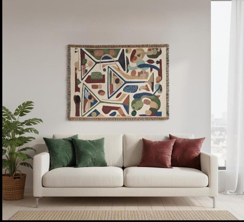 May include: A rectangular woven wall tapestry featuring an abstract pattern of geometric shapes and lines in shades of green, blue, red, and tan. The textile piece has a fringed border on all four sides and is displayed horizontally.