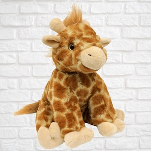 May include: A plush giraffe toy with brown and tan fur, sitting on a white brick background. The giraffe has a long neck, large ears, and a friendly face.
