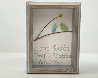 May include: A framed artwork featuring two blue and green glass birds perched on a twig. The artwork is inscribed with the text "Love Birds Troy ♥ Gabbie 9/19/2020".