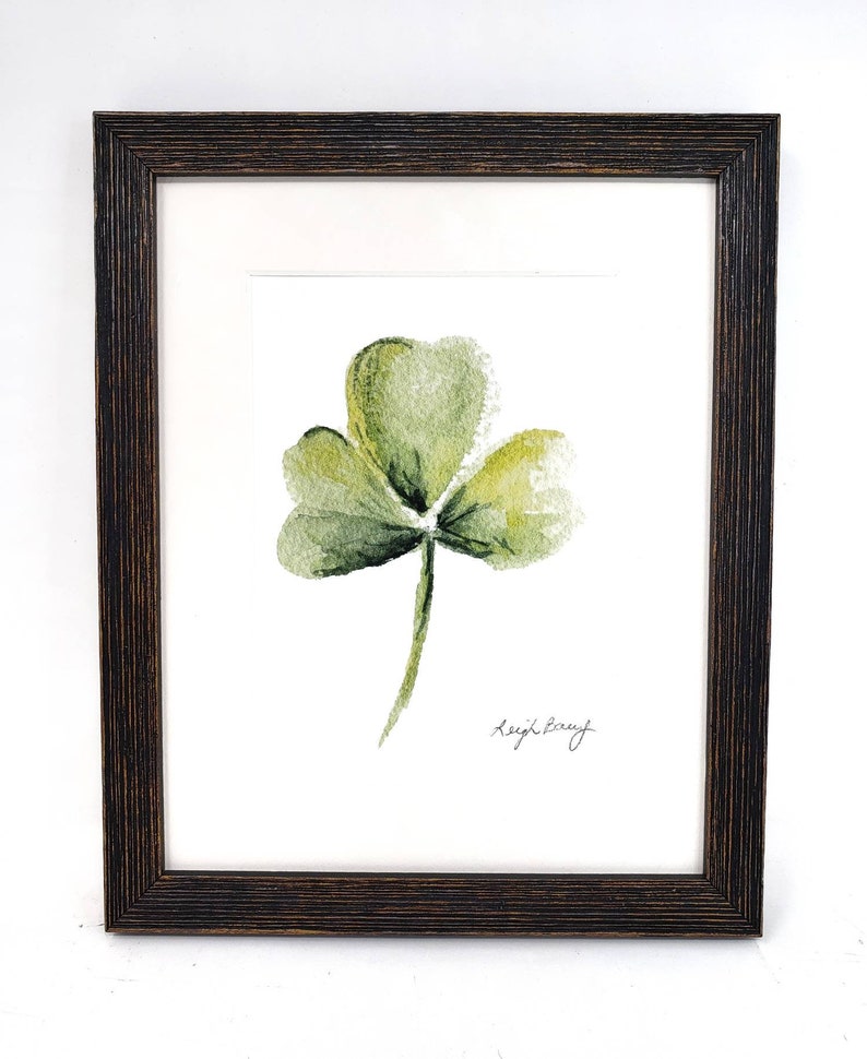 Puede incluir: Pintura a la acuarela de un tr&eacute;bol verde de tres hojas, firmada "Leigh Barry", enmarcada en un marco de madera marr&oacute;n oscuro. El tr&eacute;bol est&aacute; centrado sobre un fondo blanco.