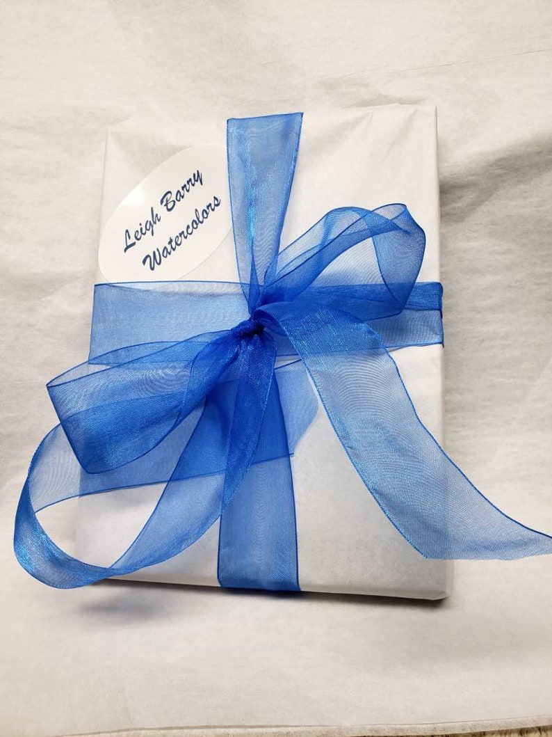 May include: A present wrapped in white paper, secured with a vibrant blue ribbon tied in a bow. An oval label with the text "Leigh Barry Watercolors" is attached. The background is a light, textured surface.