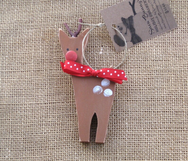 May include: A wooden reindeer ornament with a red and white polka dot bow, a red nose, and white paint spots. The ornament is hanging from a string.
