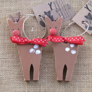 May include: Two wooden reindeer ornaments with red and white polka dot bows. The reindeer are brown with white spots and red noses. The ornaments are handmade and have a rustic look.