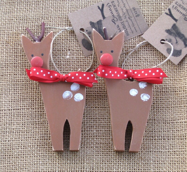 May include: Two wooden reindeer ornaments with red and white polka dot bows. The reindeer are brown with white spots and red noses. The ornaments are handmade and have a rustic look.