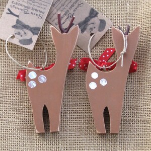 May include: Two brown wooden deer ornaments with white spots and red and white polka dot ribbon. The ornaments have twine attached for hanging.