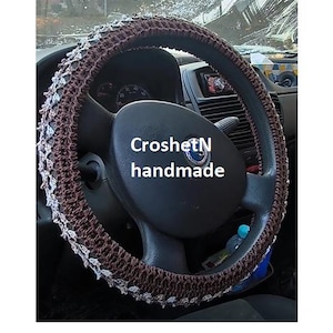 May include: A brown and white crocheted steering wheel cover with the text "CroshetN handmade".