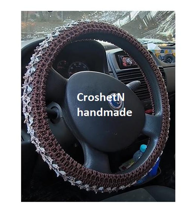 May include: A brown and white crocheted steering wheel cover with the text "CroshetN handmade".