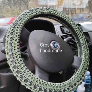 May include: Green crocheted steering wheel cover. The cover is made with a delicate open stitch pattern. The text "CroshetN handmade" is visible on the steering wheel.