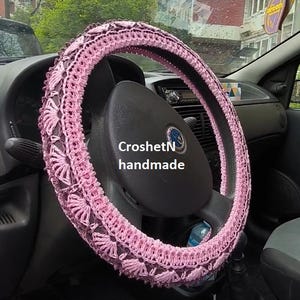 May include: Pink crocheted steering wheel cover with the text "CroshetN handmade".