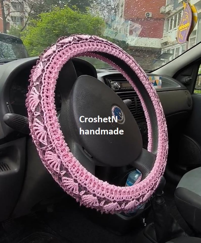 May include: Pink crocheted steering wheel cover with the text "CroshetN handmade".