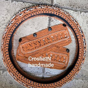 May include: A crocheted steering wheel cover in orange and black with a matching crocheted hand warmer. The hand warmer has the text "CroshetN handmade" on it.