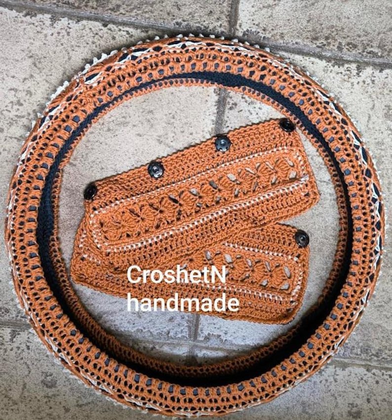 May include: A crocheted steering wheel cover in orange and black with a matching crocheted hand warmer. The hand warmer has the text "CroshetN handmade" on it.