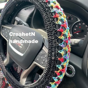 May include: A black crochet steering wheel cover with a colorful rainbow design. The cover is handmade and has the text "CroshetN handmade" on it.
