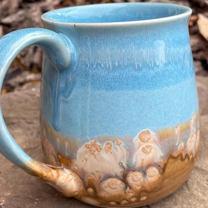 May include: A blue and brown ceramic mug with a rounded body and a handle. The mug has a light blue glaze with brown and white accents.