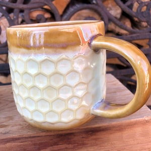 May include: A ceramic mug with a honeycomb pattern in a light yellow colour. The mug has a brown rim and handle.