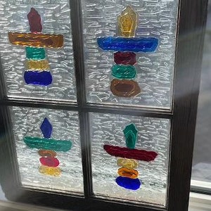 May include: A stained glass window with four panes, each featuring a colourful abstract design. The designs are made up of various shapes and colours, including red, orange, yellow, green, blue, and purple.