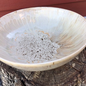 May include: A large, white ceramic bowl with a speckled, brown glaze. The bowl has a wide, shallow shape and a slightly uneven rim.