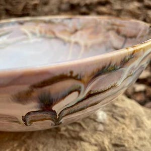 May include: A large, white ceramic bowl with brown and iridescent swirls. The bowl is made in a marbled style and has a smooth, glossy finish.
