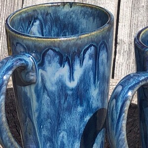 May include: Two blue and white ceramic mugs with a drip glaze finish. The mugs have a handle and are tall and slender.