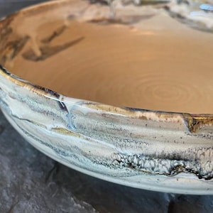 May include: A large, ceramic serving bowl with a white glaze and brown and black marbling. The bowl has a wide, rounded rim and a slightly flared lip.