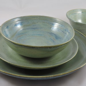 May include: A set of three green ceramic bowls with a blue glaze. The bowls are nested inside each other, with the largest bowl on the bottom and the smallest bowl on top.