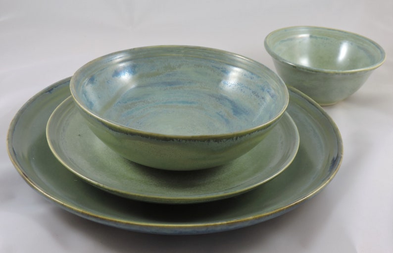 May include: A set of three green ceramic bowls with a blue glaze. The bowls are nested inside each other, with the largest bowl on the bottom and the smallest bowl on top.