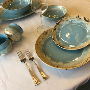 May include: A table setting with blue and white ceramic dinnerware, including a large plate, a smaller plate, a bowl, and two mugs. Two silver forks are placed on the table.