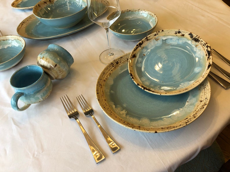 May include: A table setting with blue and white ceramic dinnerware, including a large plate, a smaller plate, a bowl, and two mugs. Two silver forks are placed on the table.