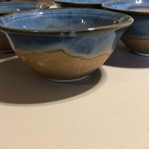 May include: Four ceramic bowls with a blue and brown glaze. The bowls are all the same size and shape, and they are arranged in a row.