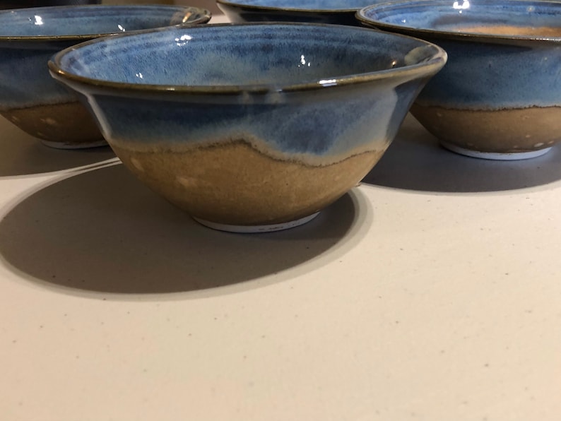 May include: Four ceramic bowls with a blue and brown glaze. The bowls are all the same size and shape, and they are arranged in a row.