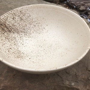 May include: A white ceramic bowl with a speckled brown glaze. The bowl is round and has a wide rim.