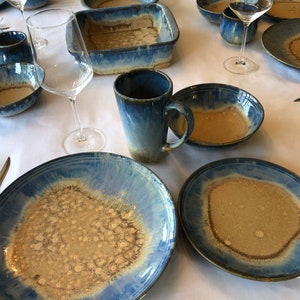 May include: A set of blue and brown ceramic dinnerware with a speckled glaze. The set includes plates, bowls, and mugs.