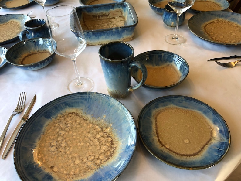 May include: A set of blue and brown ceramic dinnerware with a speckled glaze. The set includes plates, bowls, and mugs.