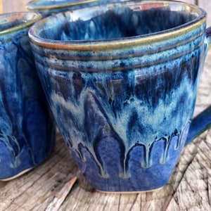 May include: Two blue ceramic mugs with a white and blue marbled glaze. The mugs have a rounded shape and a handle.