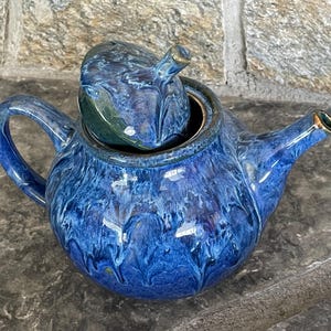 May include: A blue and green ceramic teapot with a swirling pattern. The teapot has a lid and a spout.