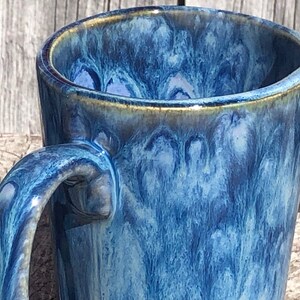May include: A blue ceramic mug with a marbled glaze. The mug has a wide, rounded handle and a slightly flared rim.