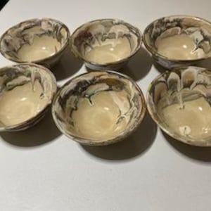 May include: Set of six ceramic bowls with a marbled glaze in shades of brown, white, and gray. The bowls have a rounded shape and a slightly flared rim.