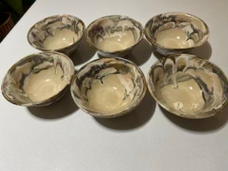 May include: Set of six ceramic bowls with a marbled glaze in shades of brown, white, and gray. The bowls have a rounded shape and a slightly flared rim.