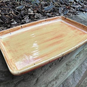 May include: A rectangular ceramic tray featuring a glossy finish with a warm colour palette of cream, yellow, and burnt orange streaks. The tray has slightly raised edges and a smooth, reflective surface with visible brushstroke patterns.