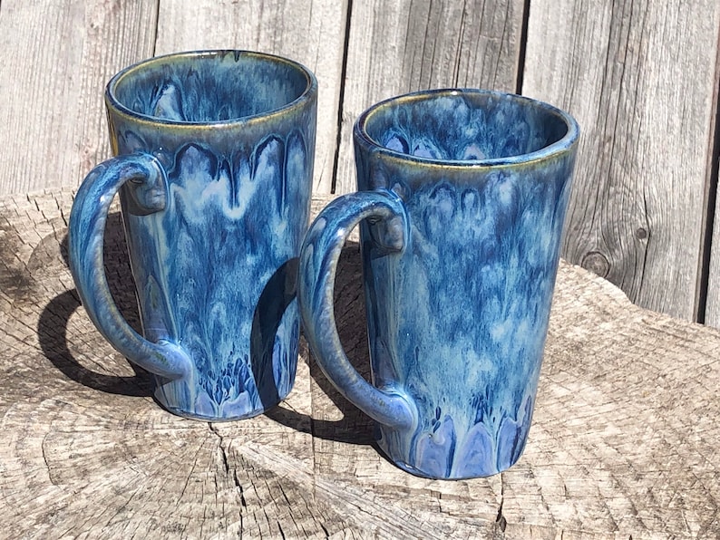May include: Two blue ceramic mugs with white and blue marbled glaze. The mugs have a rounded shape and a handle on the side.
