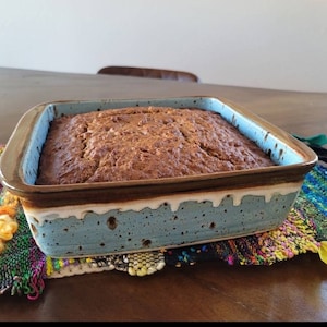 May include: A brown loaf of bread baked in a blue and brown speckled ceramic baking dish. The dish has a white glaze around the top edge.