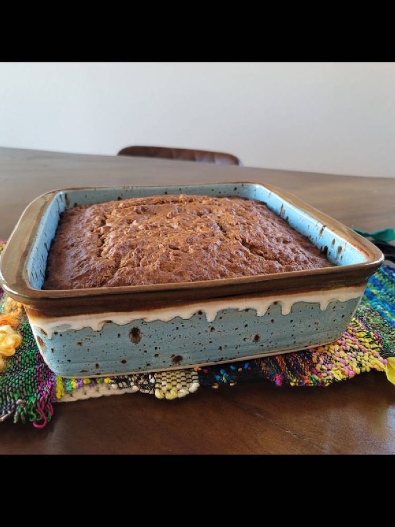 May include: A brown loaf of bread baked in a blue and brown speckled ceramic baking dish. The dish has a white glaze around the top edge.