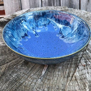 May include: A large, blue ceramic bowl with a white and blue glaze. The bowl has a slightly rippled edge and a gold rim.