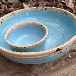 May include: A blue ceramic serving dish with a smaller bowl inside. The dish has a white rim with brown speckles.