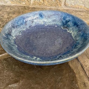 May include: A large, round, blue ceramic bowl with a white glaze. The bowl has a slightly rippled edge and a smooth, glossy finish.