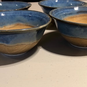 May include: Four ceramic bowls with a blue and brown glaze. The bowls are all the same size and shape, and they are arranged in a row.