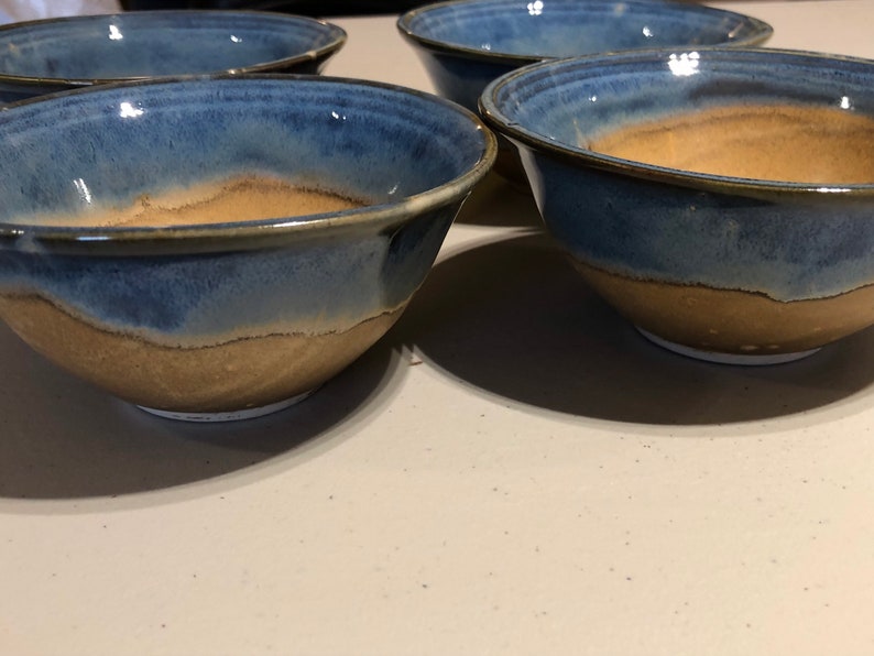 May include: Four ceramic bowls with a blue and brown glaze. The bowls are all the same size and shape, and they are arranged in a row.